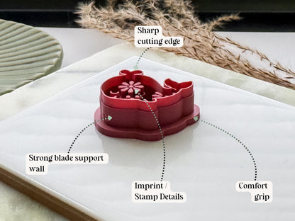 Side view of a whale-shaped polymer clay cutter in deep red PLA, highlighting the sharp cutting edge, reinforced support wall, embossed stamp details and comfortable grip handle. Displayed on a white tile with decorative dried grasses.