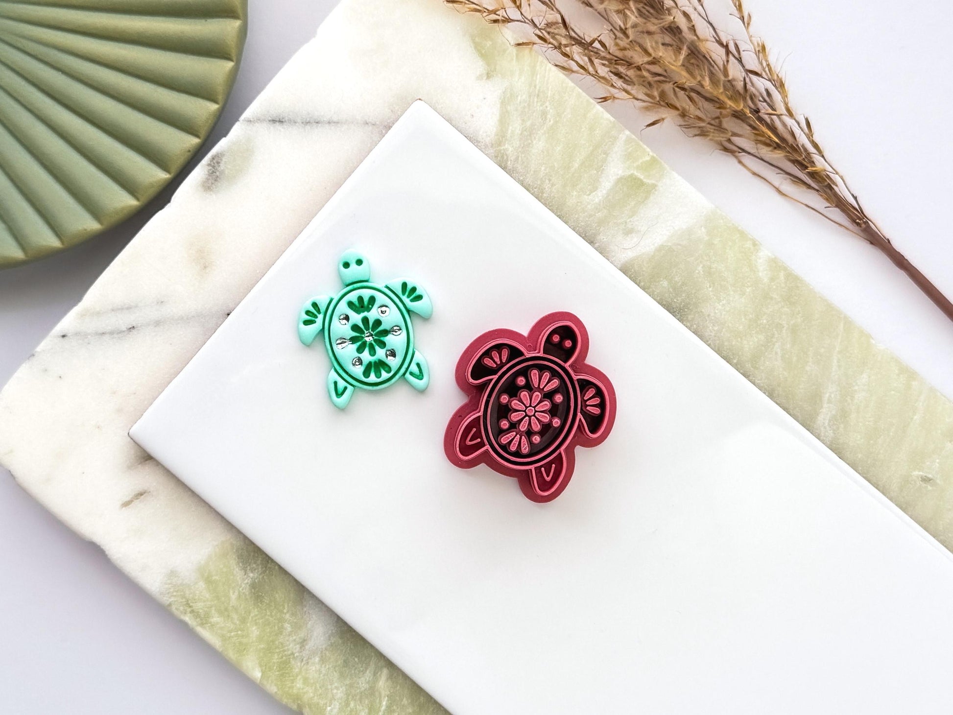 Sea turtle polymer clay cutter with decorative floral stamp pattern displayed next to a mint green clay impression. UK-made crafting tool for polymer clay, fondant, jewellery and decorative craft projects.