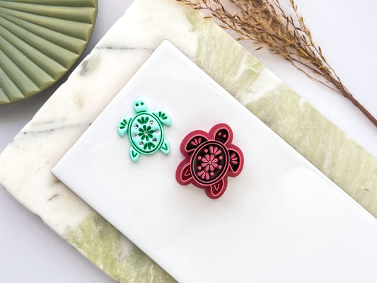 Sea turtle polymer clay cutter with decorative floral stamp pattern displayed next to a mint green clay impression. UK-made crafting tool for polymer clay, fondant, jewellery and decorative craft projects.