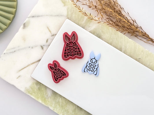 Fluffy moth polymer clay cutters in two sizes displayed beside a matching pale blue clay cut-out. The moth design features embossed wing and body details and is shown on a white ceramic tile with a marble-effect background.