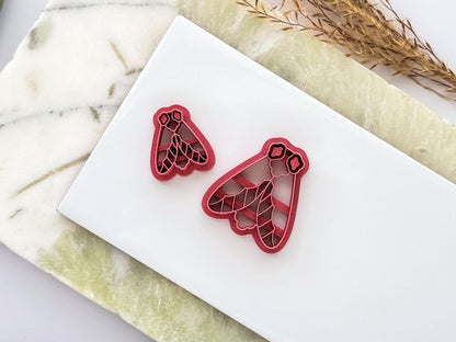 Set of two moth-shaped polymer clay cutters in different sizes, featuring intricate wing and floral-inspired stamp details. Displayed on a white ceramic tile with a marble-effect background for size comparison.