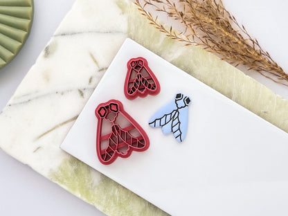 Two simple moth-shaped polymer clay cutters with detailed stamp pattern alongside a blue clay impression. UK-made crafting tools for polymer clay, fondant, jewellery making and creative craft projects.