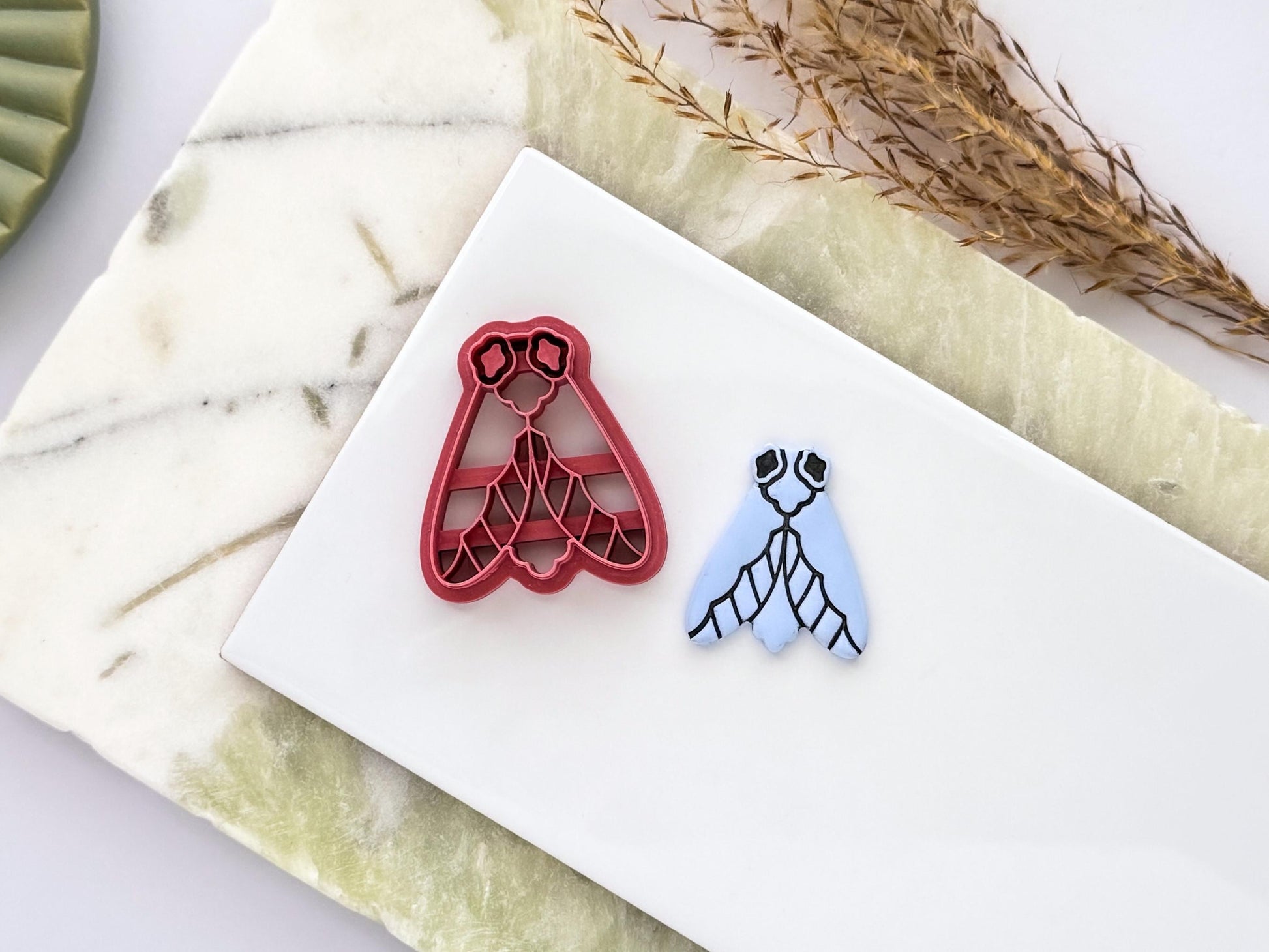 Moth polymer clay cutter with embossed details, shown with matching clay cut-out. Insect-themed clay tool for earrings, jewellery, fondant decorating and handmade craft projects.