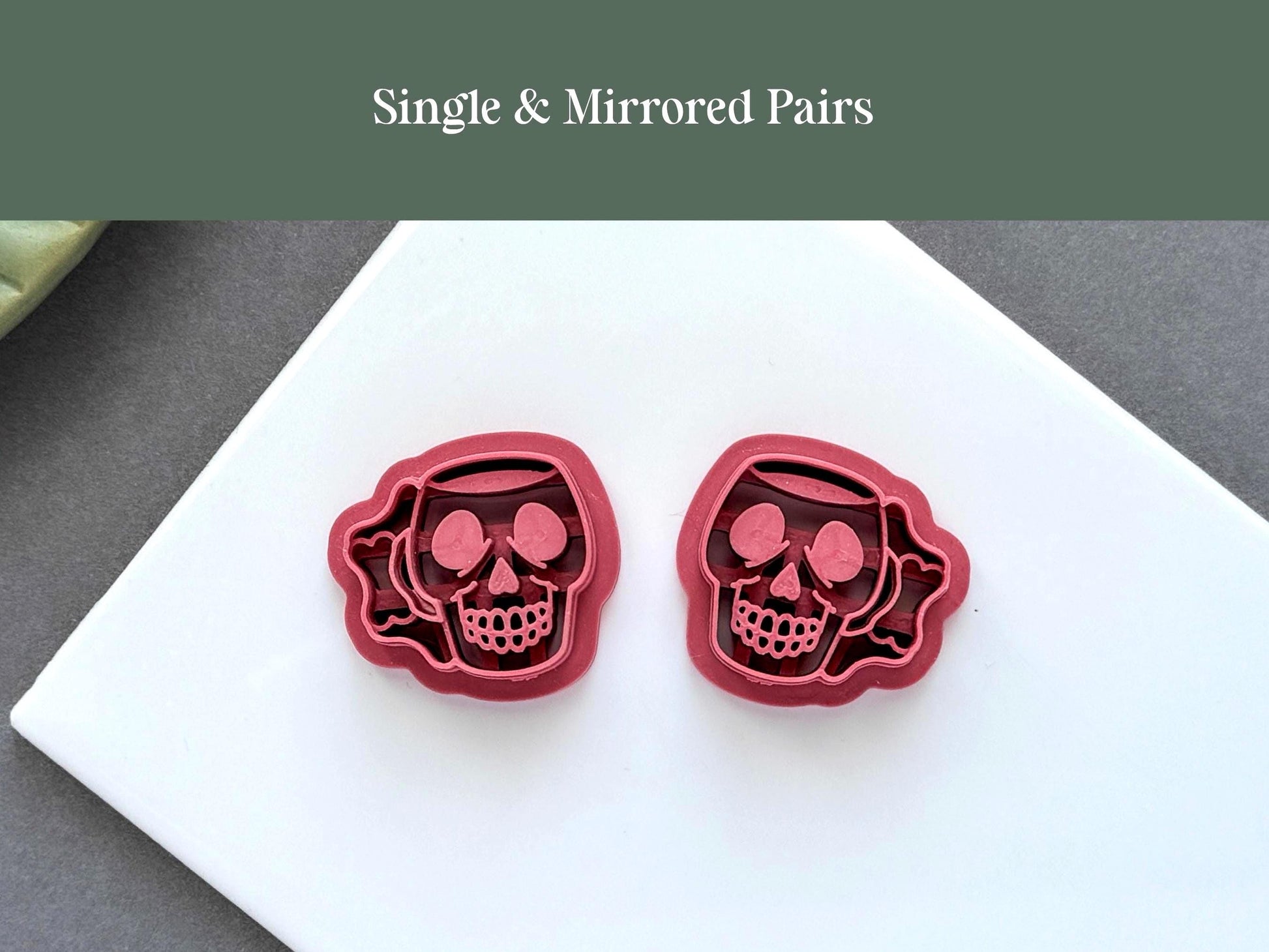 Matching left and right skull mug polymer clay cutters with detailed embossed skull faces, displayed on a white ceramic tile. Ideal for creating mirrored Halloween earrings and jewellery.