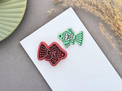 Folk art fish polymer clay cutter with detailed floral and fin designs, shown next to a mint green clay cut-out. UK-made clay tool for earrings, jewellery making, fondant decorating and handmade craft projects.