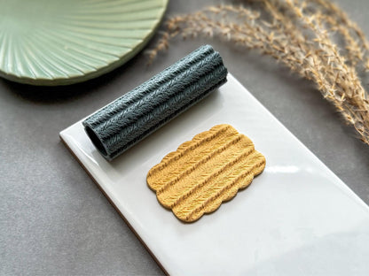 Feather texture roller for polymer clay with sample clay impression on white ceramic tile.