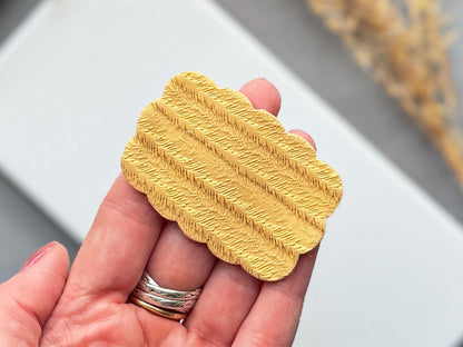 Textured polymer clay slab with feather pattern held in hand to show scale.
