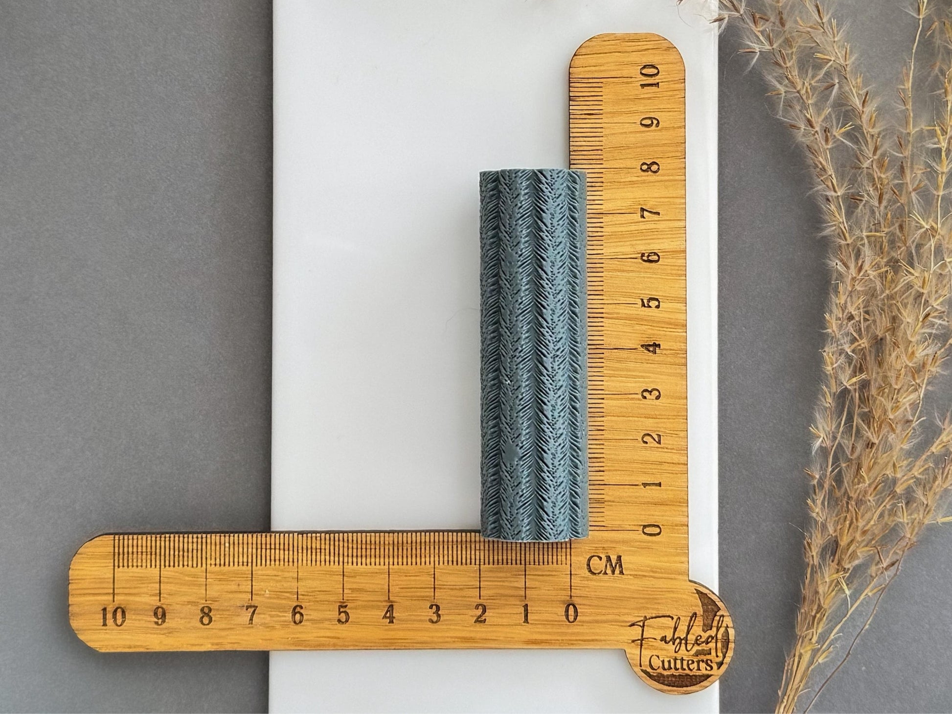 Feather texture roller shown beside centimetre ruler to display size for polymer clay projects.