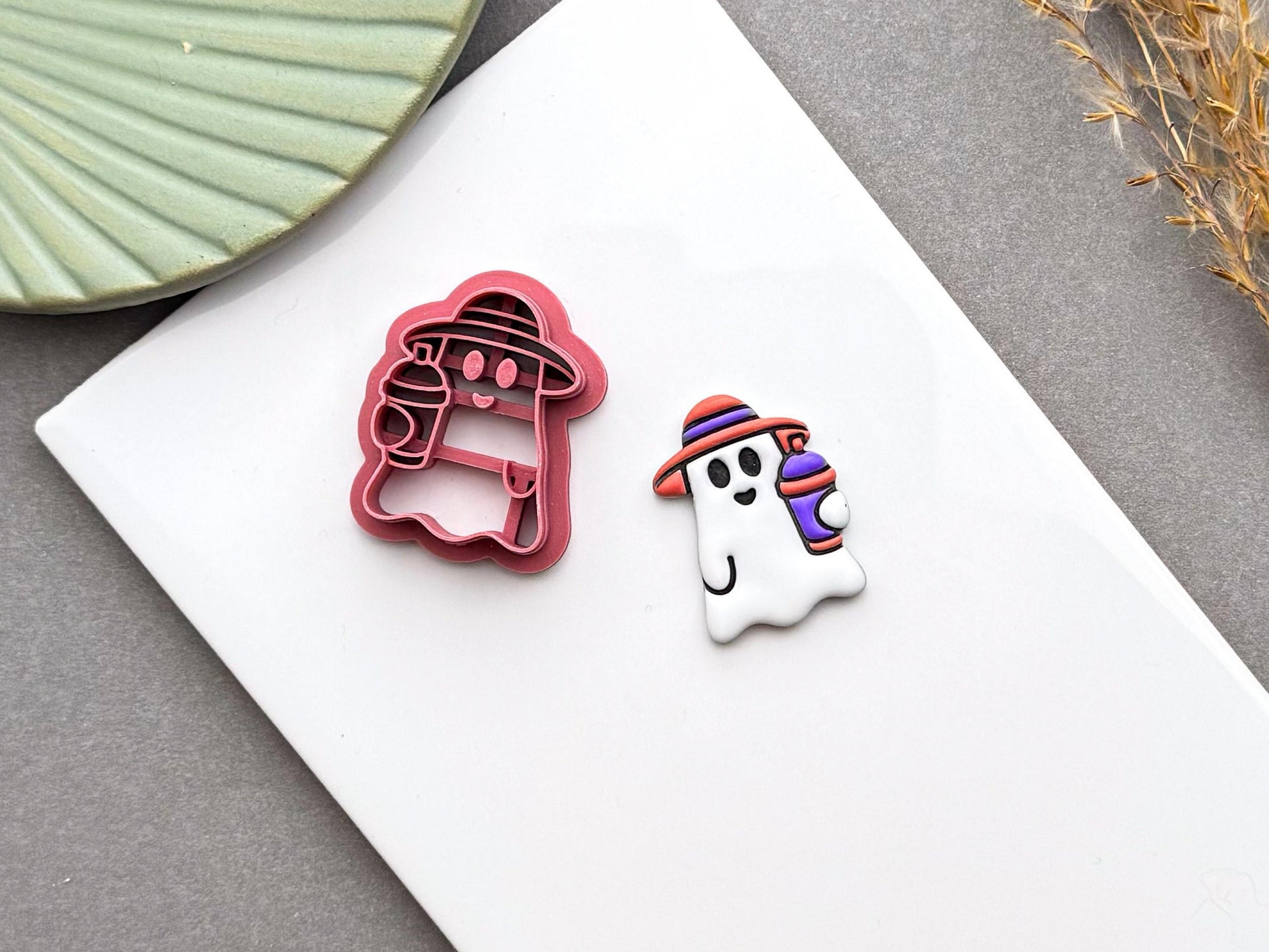 Cute summer ghost polymer clay cutter displayed beside a finished ghost earring with a striped smoothie cup.