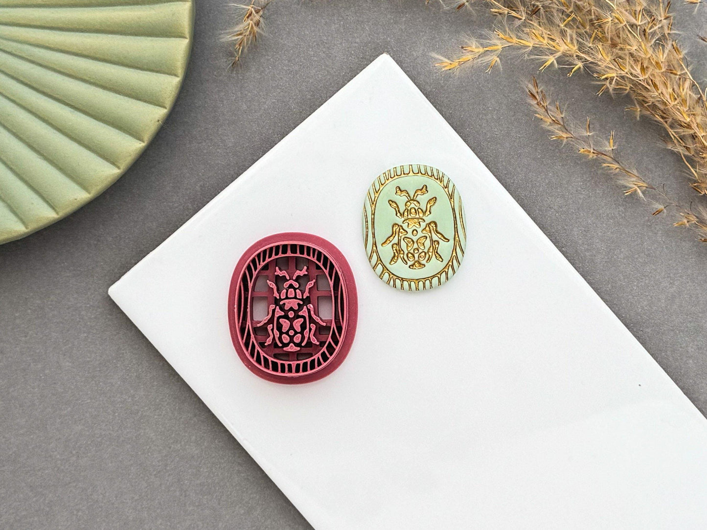 Decorative beetle polymer clay cutter displayed beside a matching finished polymer clay embellishment featuring an ornate beetle design within a decorative wood grain inspired border.