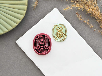 Decorative beetle polymer clay cutter displayed beside a matching finished polymer clay embellishment featuring an ornate beetle design within a decorative wood grain inspired border.