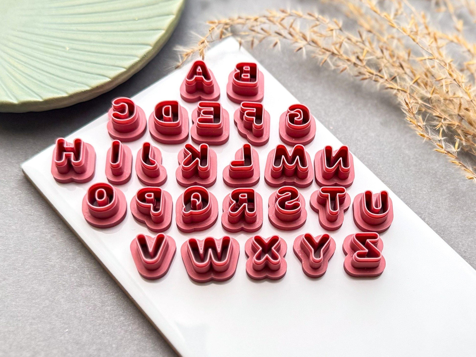 Complete uppercase alphabet polymer clay letter cutter set from A to Z displayed on a white tile, featuring rounded bubble-style lettering for clay crafts.