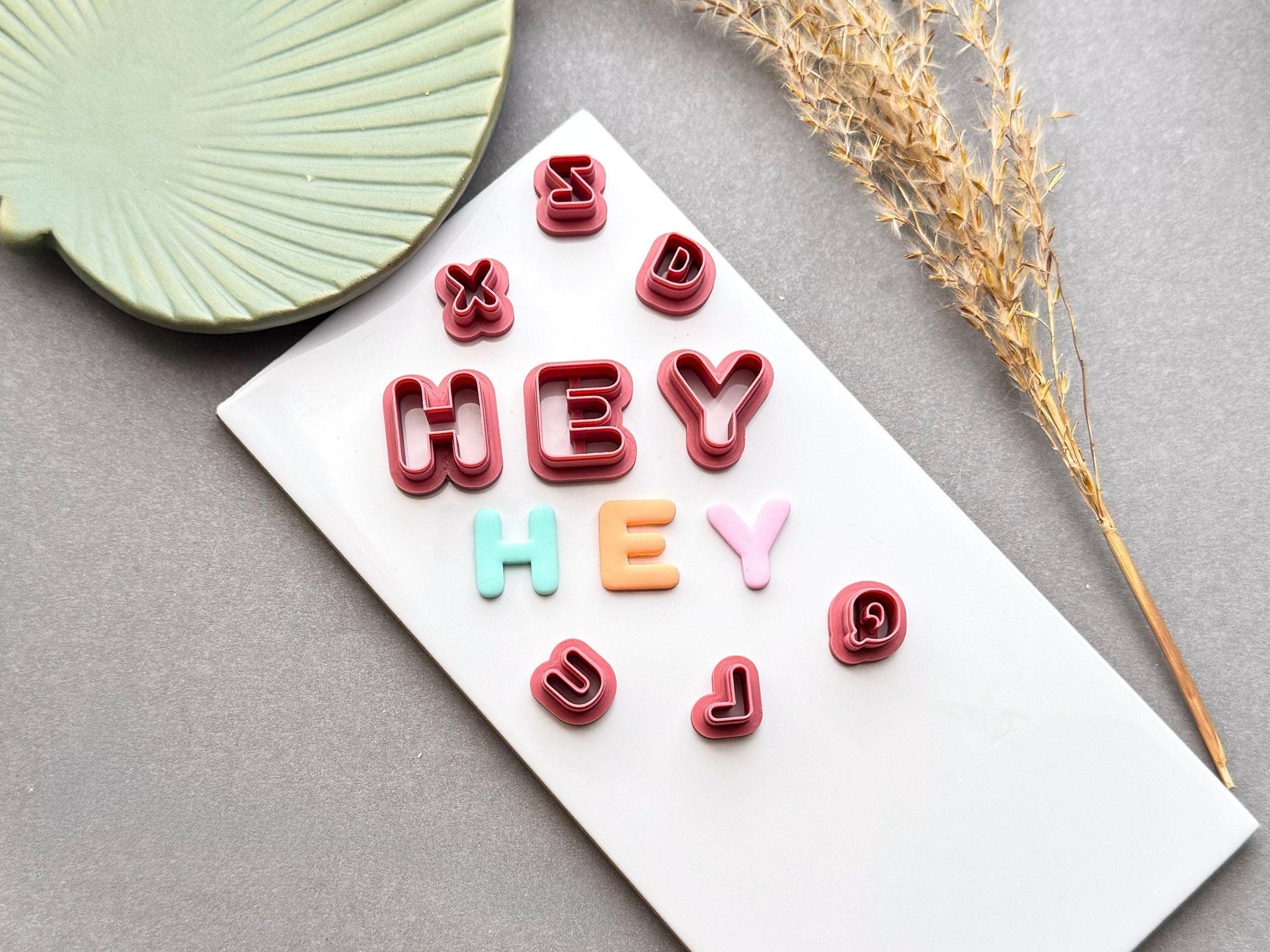 Uppercase alphabet polymer clay letter cutters spelling "HEY" with matching pastel clay letters and coordinating lowercase cutters displayed on a white tile.
