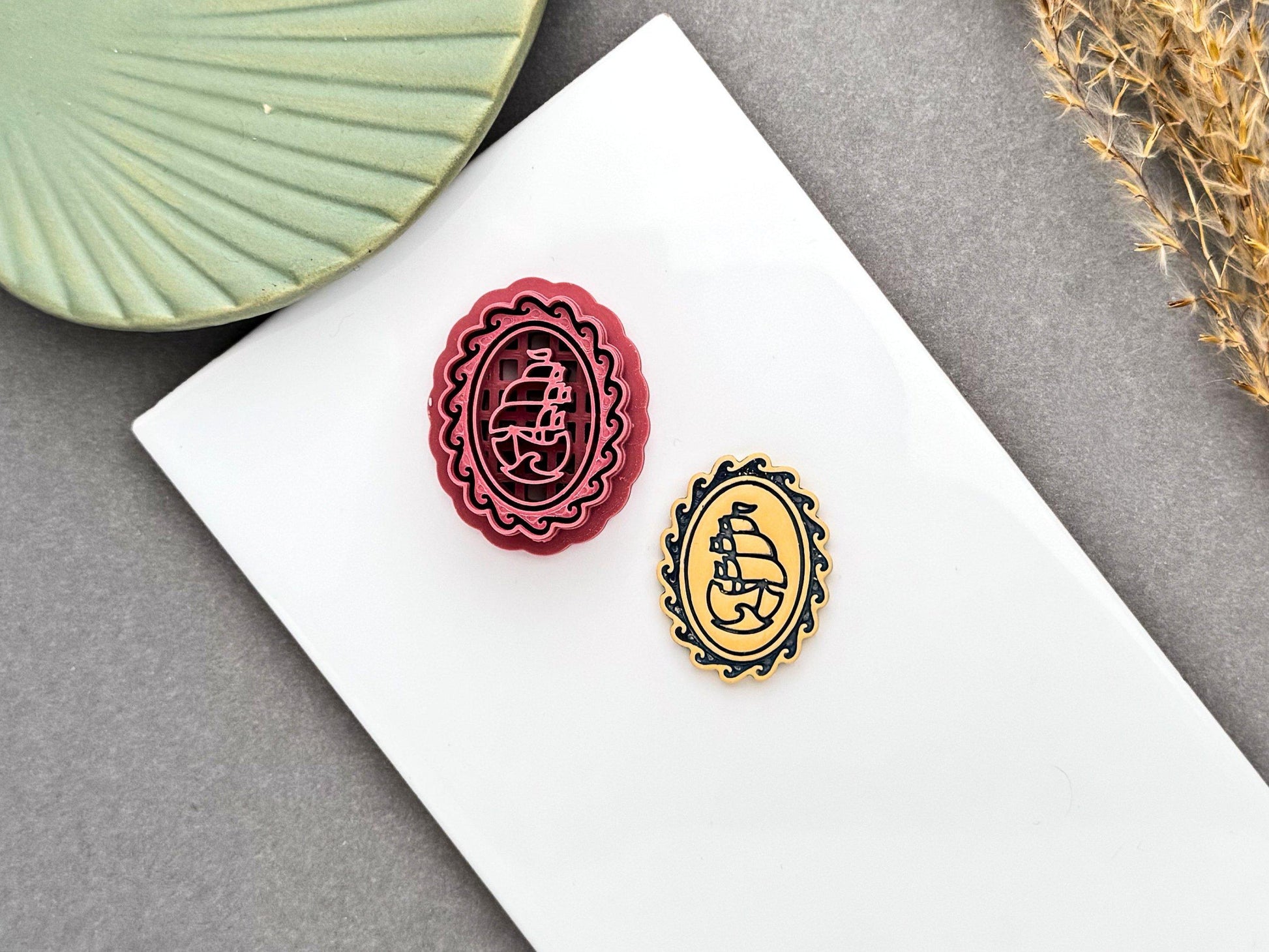 burgundy polymer clay cutter featuring an ornate oval cameo frame with a vintage sailing ship design, displayed beside the finished polymer clay cut-out. The image highlights the detailed imprint and finished nautical design.