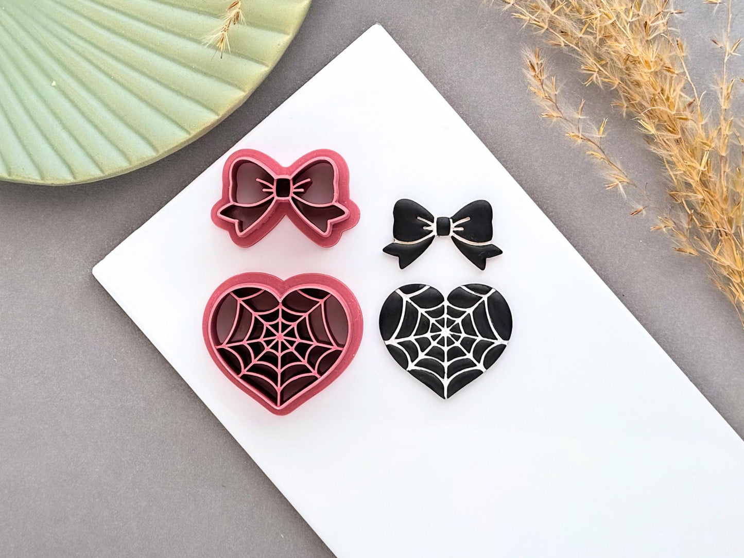 Spider web heart and bow polymer clay cutters displayed alongside finished polymer clay samples, featuring gothic spider web designs for creating Halloween jewellery, spooky charms and alternative craft projects.