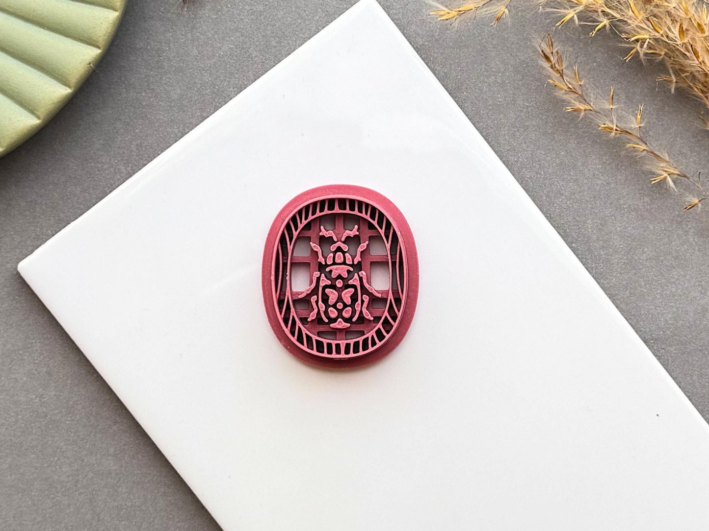 Decorative beetle polymer clay cutter featuring an ornate beetle design within a decorative Egyptian-inspired border, displayed on a white tile.
