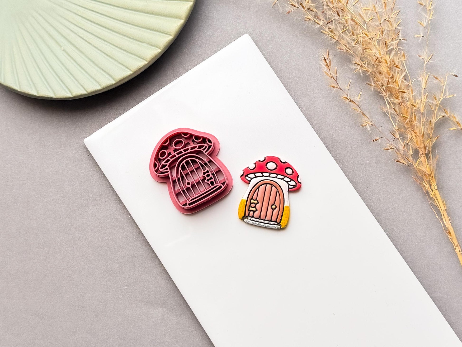 Mushroom cottage polymer clay cutter and finished clay piece, showing a red spotted mushroom with a tiny door, on a white surface.