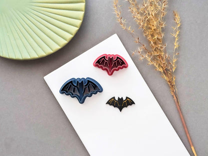Bat polymer clay cutter displayed with matching finished clay bats in different colours and sizes, featuring a simple winged bat design, perfect for Halloween, gothic and spooky clay projects.