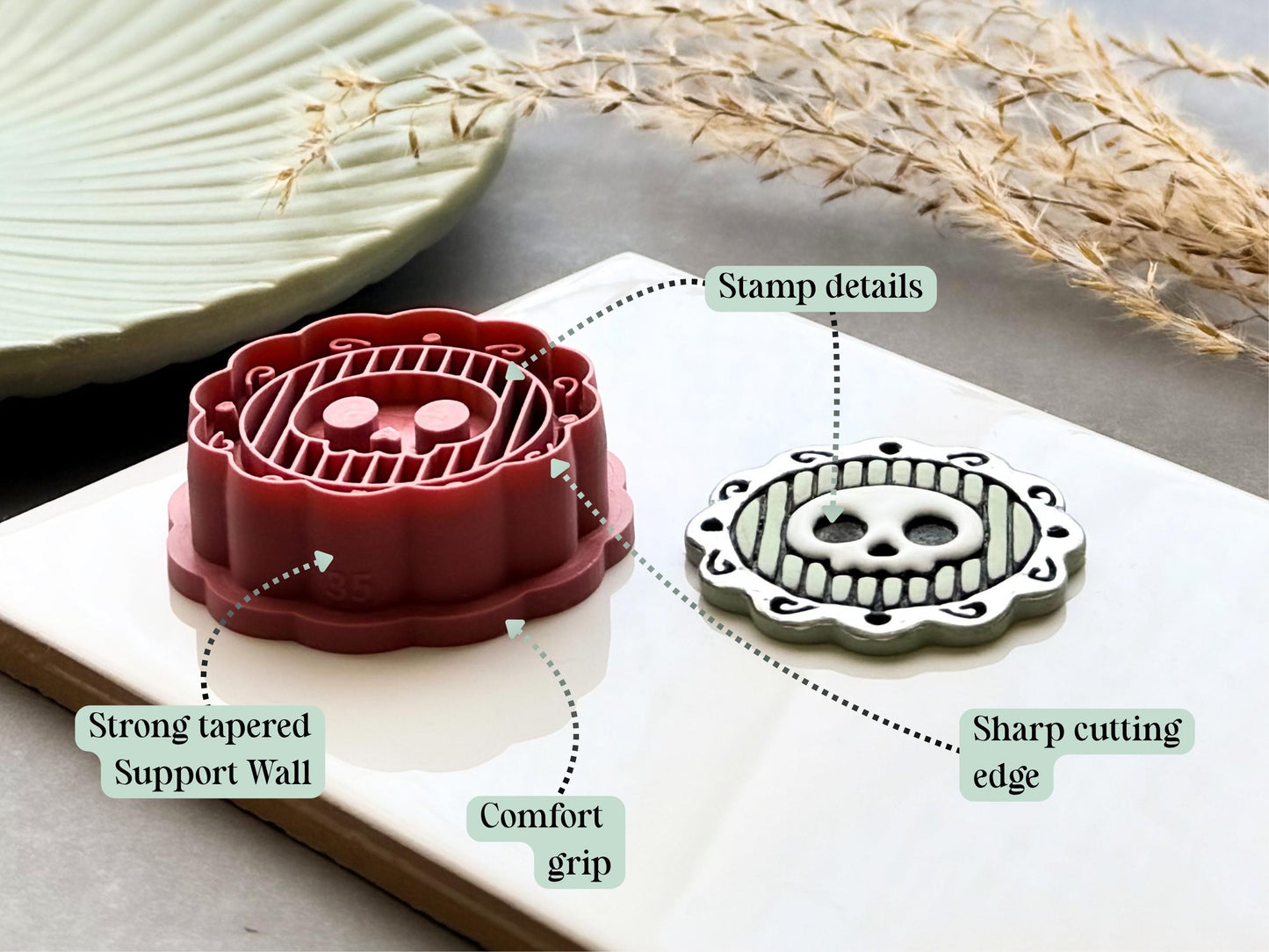 Skull frame polymer clay cutter highlighting the sharp cutting edge, comfort grip, reinforced tapered support walls and detailed embossed design, displayed alongside a finished polymer clay skull medallion sample.