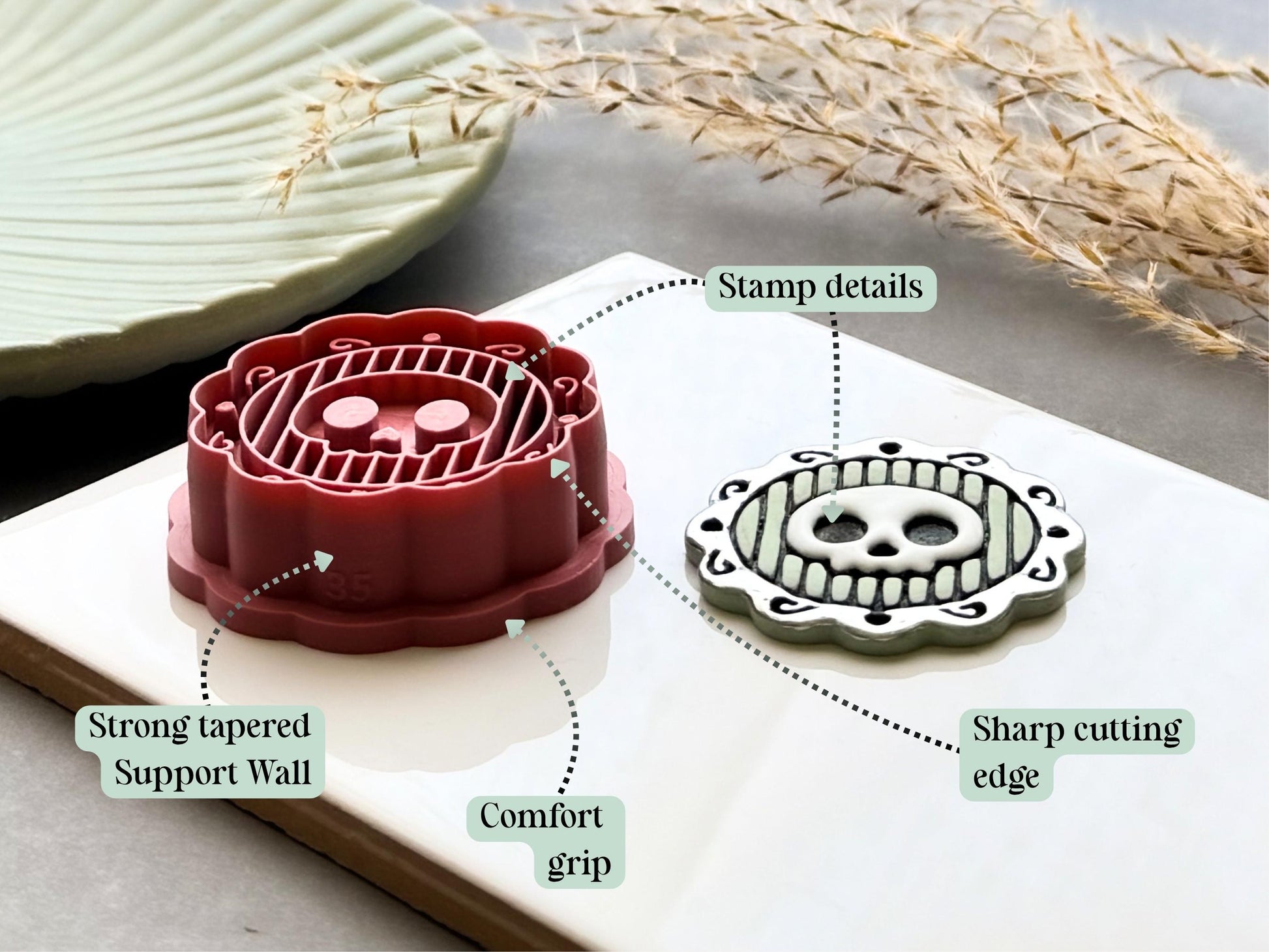 Skull frame polymer clay cutter highlighting the sharp cutting edge, comfort grip, reinforced tapered support walls and detailed embossed design, displayed alongside a finished polymer clay skull medallion sample.
