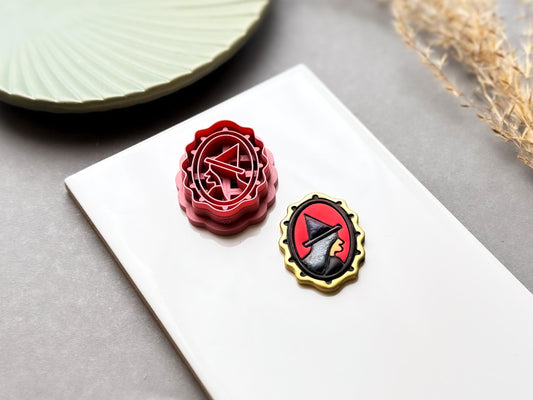Witch hat polymer clay cutter displayed beside a matching finished clay embellishment, featuring a stylised witch hat inside an ornate oval frame, perfect for Halloween, witchy, gothic and spooky clay projects.