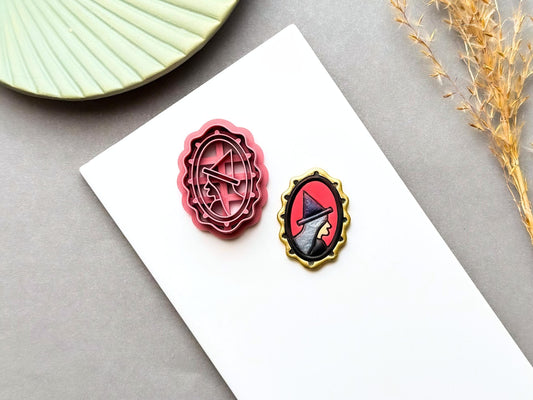 Witch hat polymer clay cutter displayed beside a matching finished clay embellishment, featuring a stylised witch hat inside an ornate oval frame, perfect for Halloween, witchy, gothic and spooky clay projects.