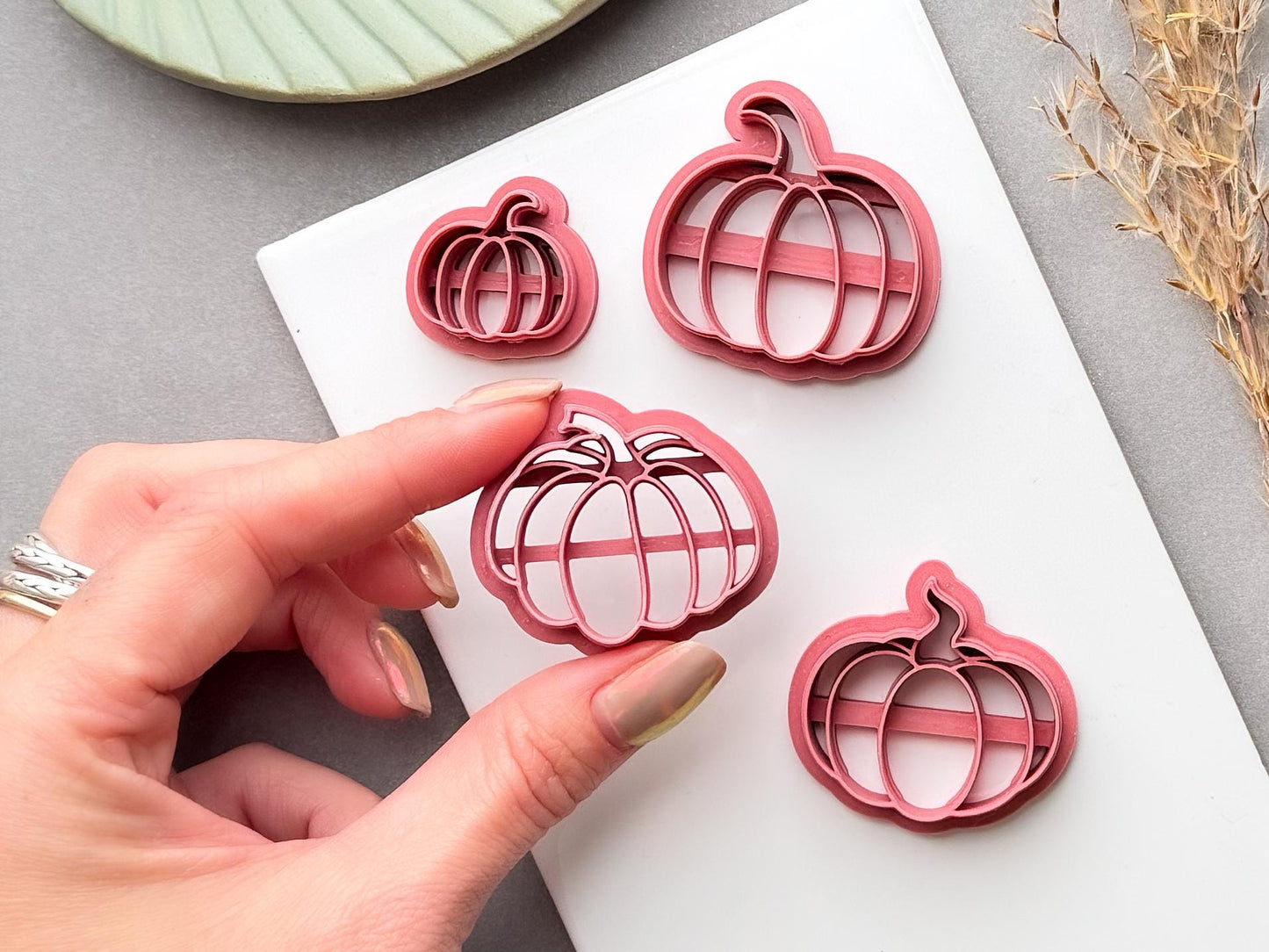 Pumpkin polymer clay cutters in multiple sizes, with one cutter held by hand to show the size and detailed pumpkin shape.