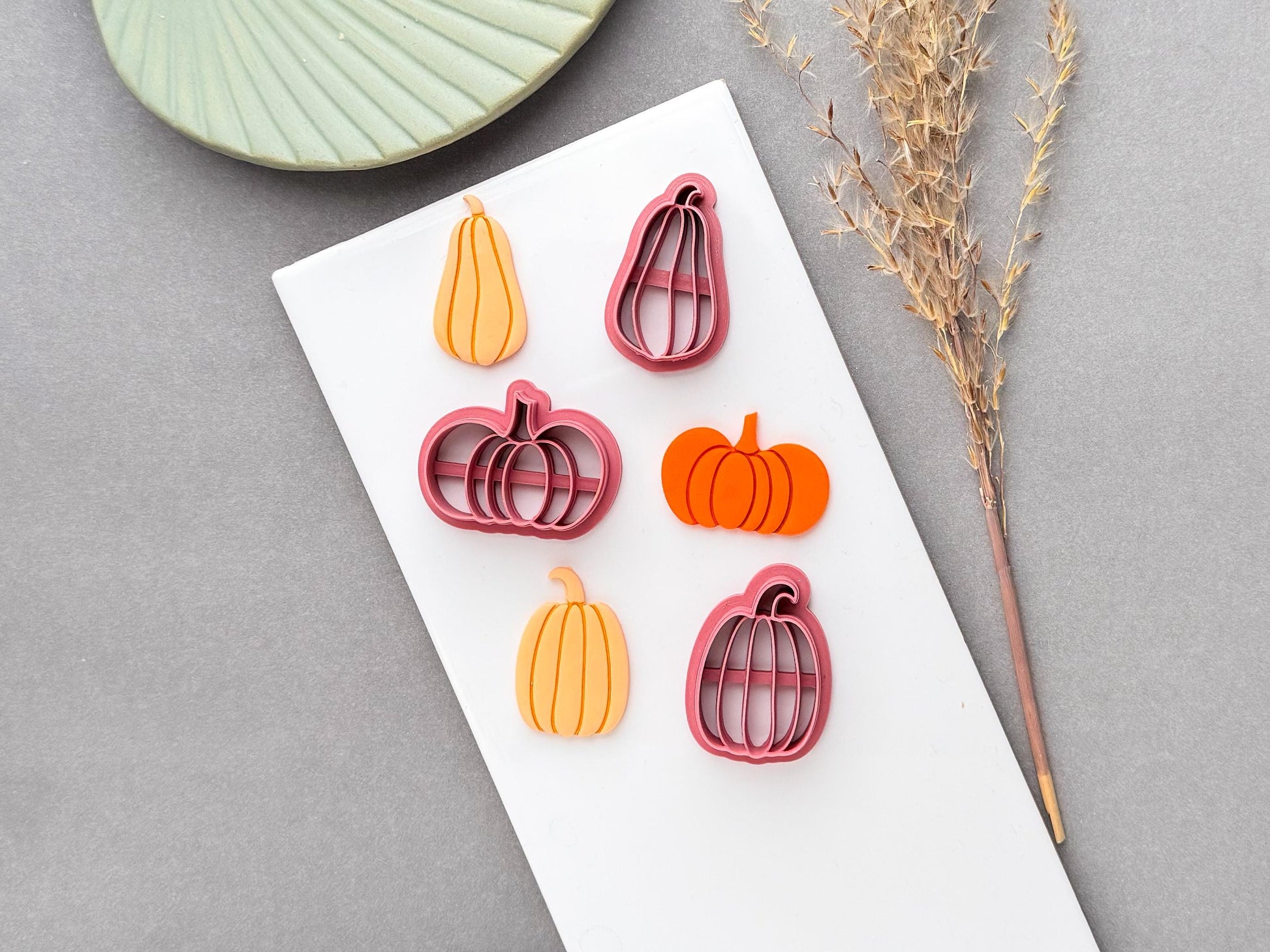 Pumpkin polymer clay cutters in multiple sizes, featuring segmented pumpkin designs and curved stems, shown alongside finished orange pumpkin clay pieces.