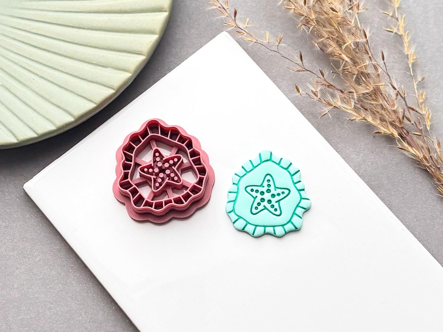 Starfish polymer clay cutter with detailed stamp design, shown beside a finished turquoise starfish clay piece on a white surface.