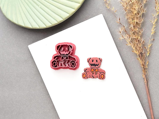 Spooky teddy bear polymer clay cutter featuring a stitched bear design with a bow tie, button-like eyes and stitched seam details, shown alongside a finished pink clay bear piece.