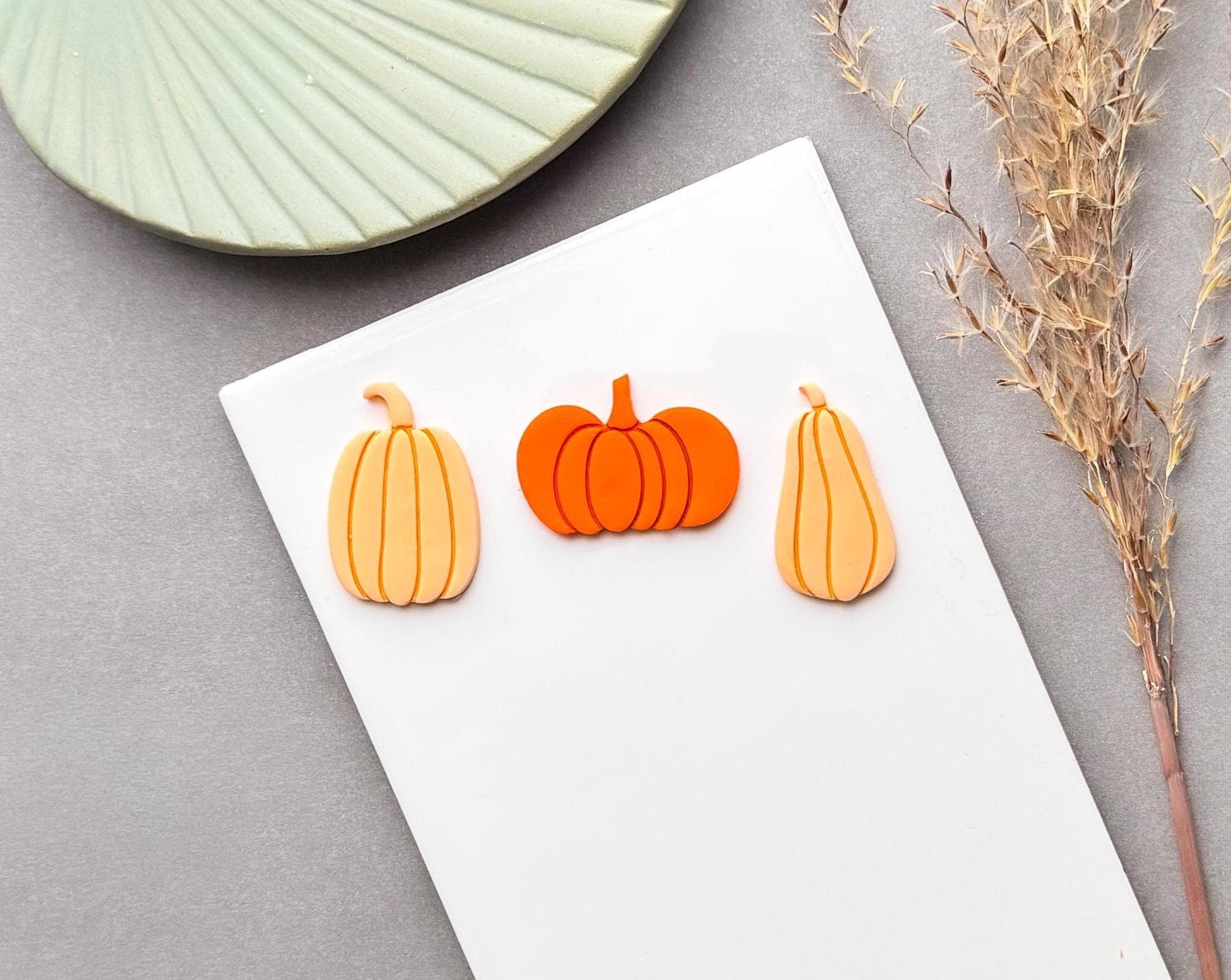 Pumpkin polymer clay cut-outs in three shapes, including a round pumpkin and two elongated pumpkin designs, shown in orange and cream clay.