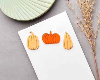 Pumpkin polymer clay cut-outs in three shapes, including a round pumpkin and two elongated pumpkin designs, shown in orange and cream clay.