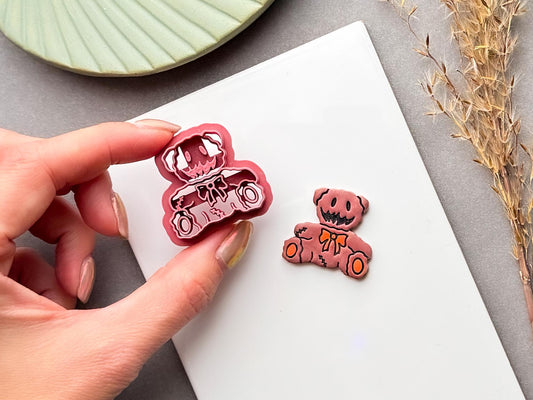 Spooky teddy bear polymer clay cutter held between fingers, featuring a stitched bear design with a bow tie, button-like eyes, stitched seams and rounded ears.