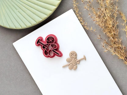 Voodoo doll clay cutter featuring a stitched figure with X-shaped eyes, button details and a long needle or pin crossing through the body, shown beside a finished polymer clay voodoo doll cut-out. Gothic, spooky and alternative Halloween-inspired design.