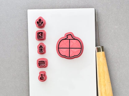 Halloween pumpkin-shaped clay cutter with five miniature witchy cutters arranged beside it: a witch’s hat, spell book, lantern, cauldron and potion bottle. Pink 3D-printed cutters displayed on a white surface with a clay sculpting tool. Gothic, witchy and Halloween-inspired design.