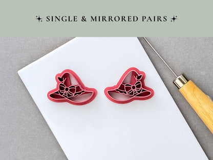 Two matching witch’s hat polymer clay cutters displayed as a mirrored pair, each featuring a decorative bow and ribbon details. Pink 3D-printed cutters shown on a white surface with a clay sculpting tool. Witchy and Halloween-inspired design.
