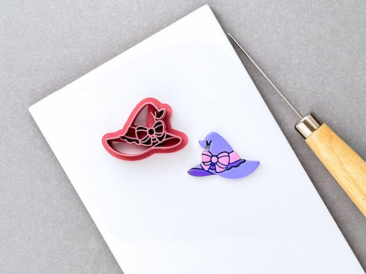 Witch’s hat clay cutter featuring a large bow and decorative ribbon details, shown beside a finished purple polymer clay witch’s hat with a pink bow. Spooky, witchy and Halloween-inspired design.