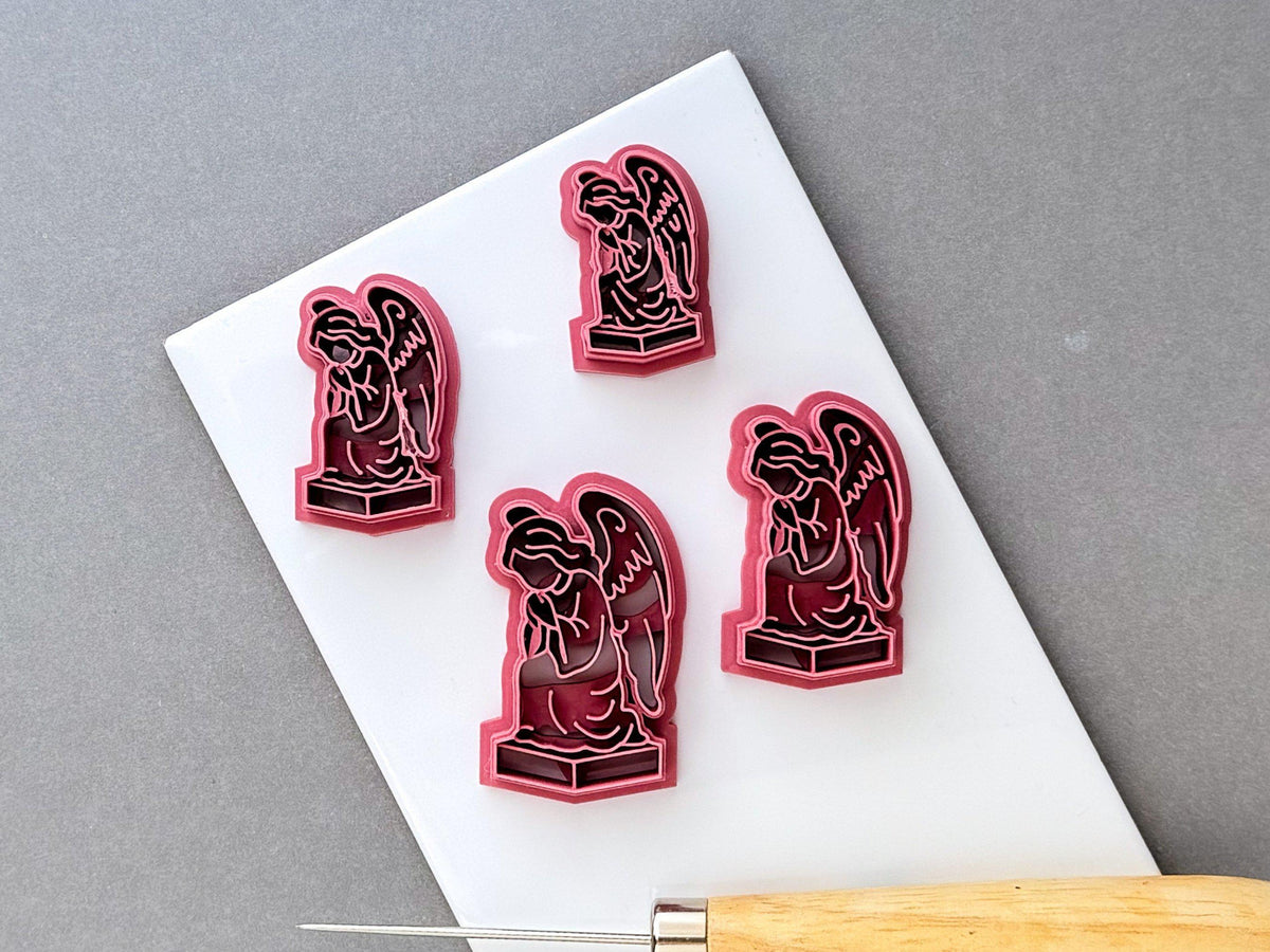 Gothic angel clay cutters displayed in four sizes, each featuring a detailed kneeling winged angel statue on a pedestal with intricate robe and feather details. Pink 3D-printed cutters arranged on a white surface.