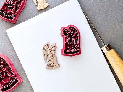 Gothic angel clay cutter featuring a detailed winged angel statue design on a pedestal, shown beside a finished cream polymer clay angel cut-out. Dark, gothic and alternative-inspired design.