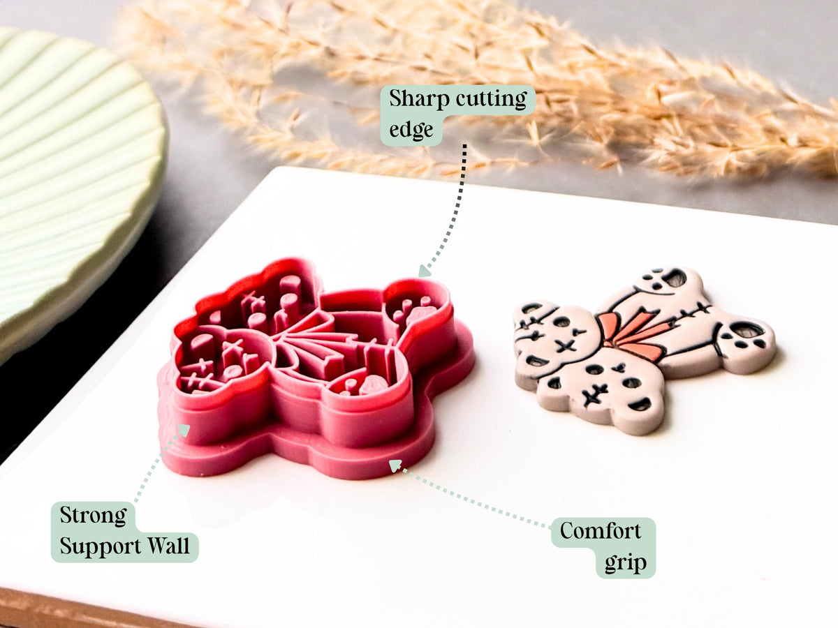 Feature graphic showing a two-headed Halloween teddy bear clay cutter with stitched patchwork details, paw pads, cross-shaped stitches and bow tie detail. Labels highlight the sharp cutting edge, strong support wall and comfortable grip, with a finished polymer clay bear shown alongside.