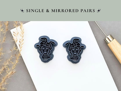 Medusa head clay cutters displayed as a mirrored pair, featuring detailed faces surrounded by flowing snake-shaped hair and decorative internal details. Dark blue 3D-printed cutters shown side by side on a white surface.