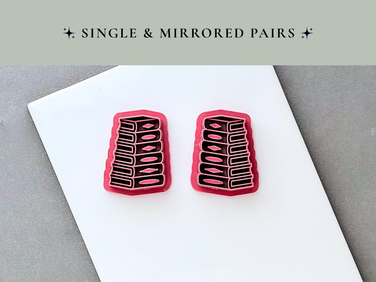 Two stack of books clay cutters displayed as a mirrored pair, each featuring detailed book spines, page edges and raised spine accents. Pink 3D-printed cutters shown on a white surface beneath a “Single & Mirrored Pairs” heading.