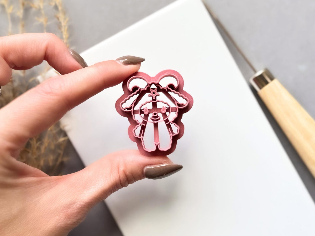 Baphomet clay cutter held between fingers, showcasing the detailed horned figure, bat-like wings, pentagram symbol, facial features and raised cutting edge.