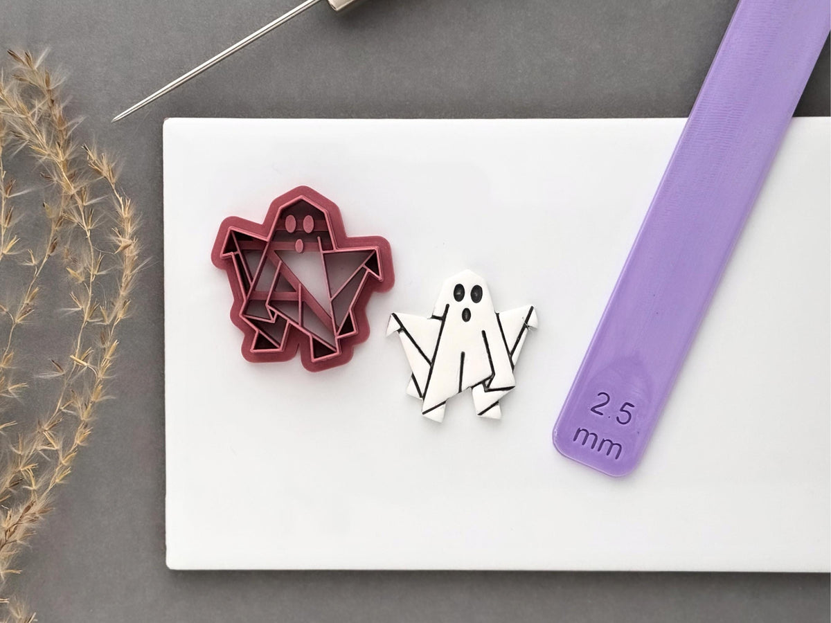 Origami ghost polymer clay cutter shown beside a finished white polymer clay origami ghost cut-out, with a 2.5 mm clay thickness guide included for scale.