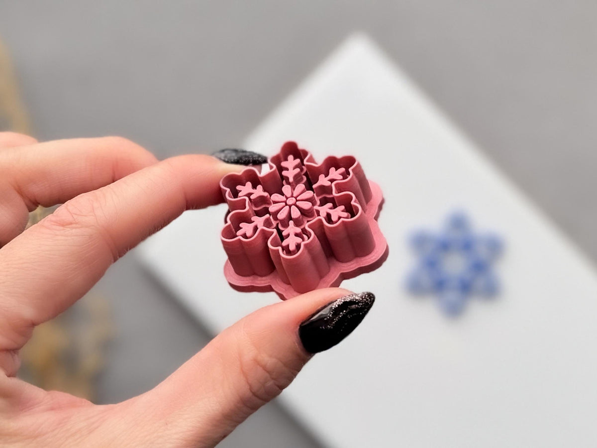 Snowflake polymer clay cutter held at an angle, showcasing the raised six-point snowflake stamp details, floral centre, deep cutting walls and sturdy support structure.