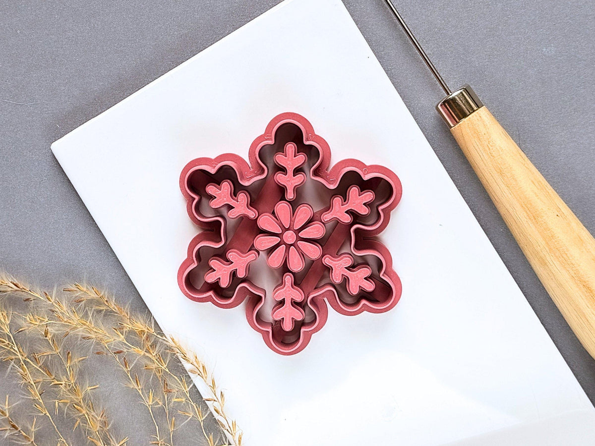 Large snowflake polymer clay ornament cutter featuring a central flower and six decorative branches with leaf-like details, displayed on a white tile.