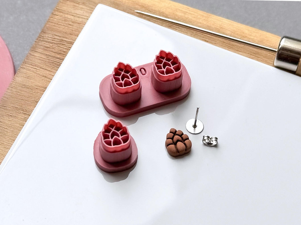 Pine cone polymer clay stamp cutter set displayed in two sizes, featuring detailed scale patterns, with joined double cutters and a separate single cutter alongside a matching finished clay pine cone embellishment and metal earring findings.