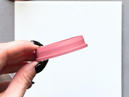 Side view of chamfered oval polymer clay cutter being held in a hand against a white tile.
