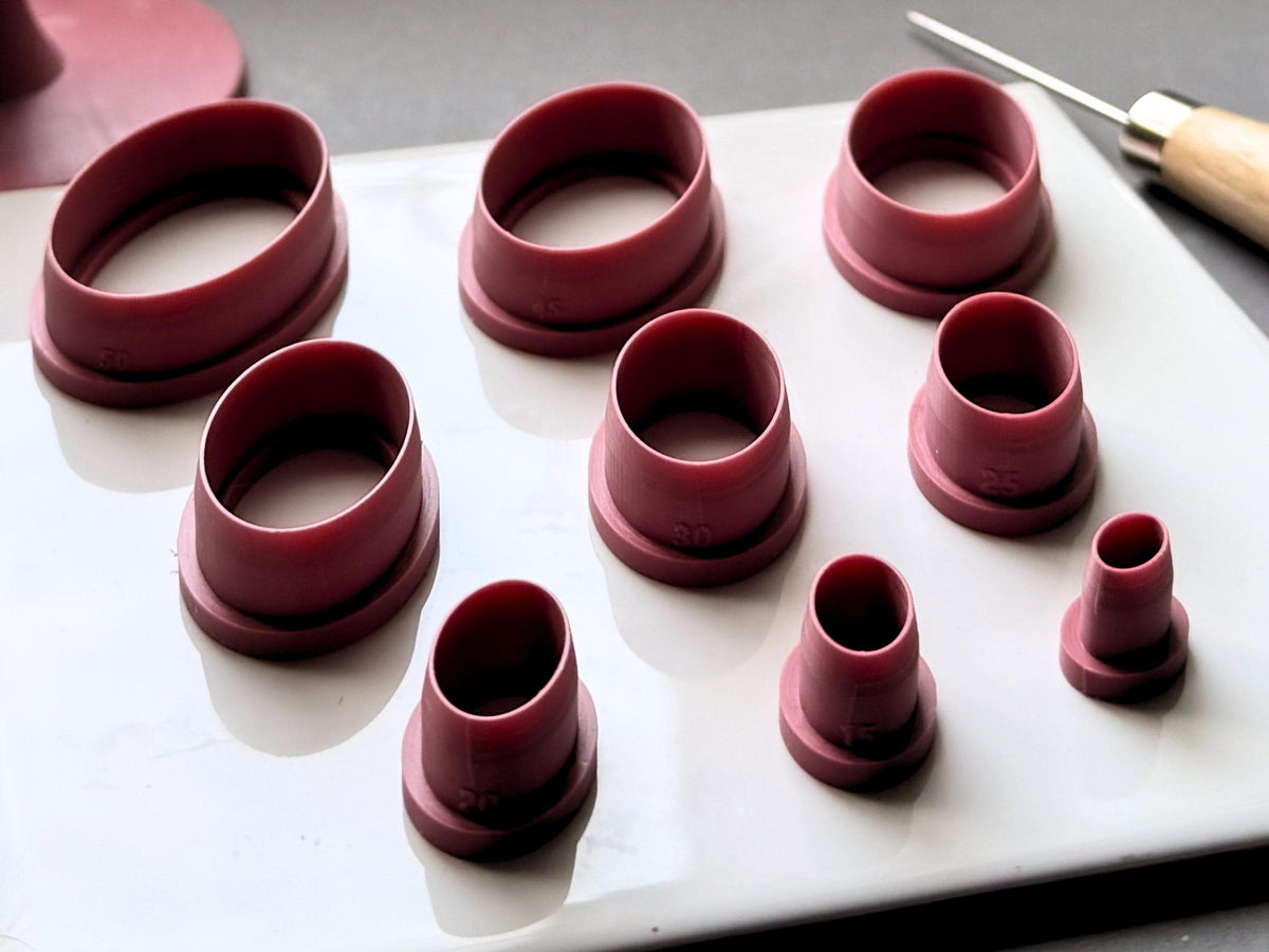 Nine oval polymer clay cutters displayed in graduated sizes on a white tile, ranging from large elongated ovals to small narrow ovals, with raised cutting walls and sturdy support bases.