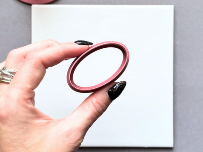 Oval polymer clay cutter held between fingers to showcase its elongated oval shape, smooth inner edge and raised cutting wall.